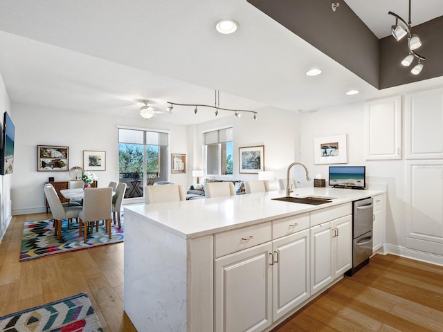 kitchen with sink, white cabinetry, hanging light fixtures, and light hardwood / wood-style flooring