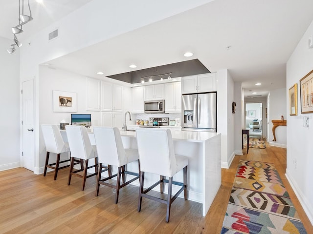 kitchen with white cabinets, hanging light fixtures, light wood-type flooring, appliances with stainless steel finishes, and a breakfast bar area