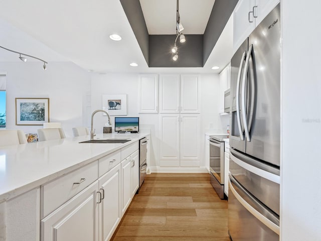 kitchen with sink, stainless steel appliances, pendant lighting, light hardwood / wood-style floors, and white cabinets