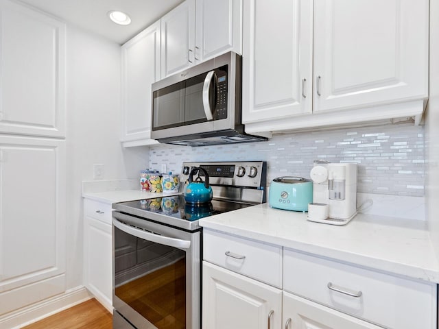 kitchen with decorative backsplash, white cabinets, stainless steel appliances, and light wood-type flooring