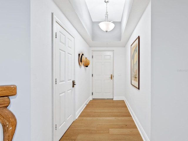 hallway with light wood-type flooring and a raised ceiling