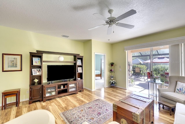 living room featuring ceiling fan, light hardwood / wood-style floors, and a textured ceiling