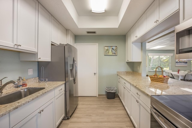 kitchen with white cabinets, light wood-type flooring, light stone countertops, and sink