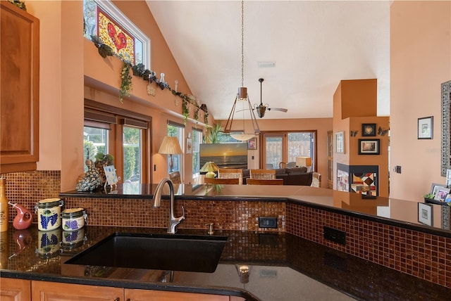 kitchen with ceiling fan, sink, tasteful backsplash, dark stone counters, and lofted ceiling