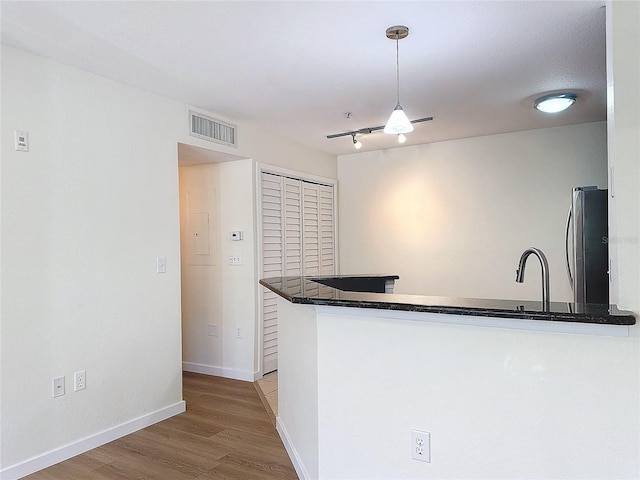 kitchen with stainless steel refrigerator, kitchen peninsula, pendant lighting, and light wood-type flooring