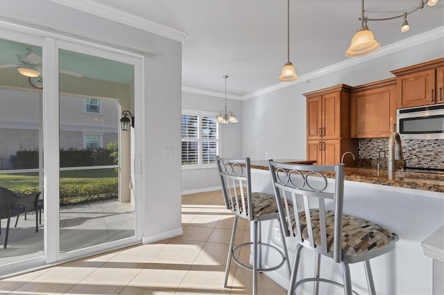 500 San Lino Cir Unit 511, Venice, FL 34292 - kitchen featuring stainless steel microwave, decorative backsplash, brown cabinetry, a kitchen breakfast bar, and ornamental molding