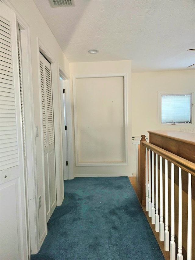 hall with a textured ceiling and dark colored carpet