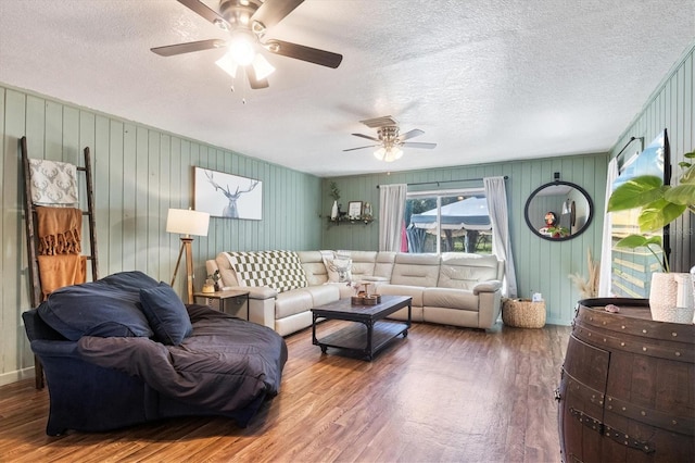 living room featuring wood-type flooring, a textured ceiling, ceiling fan, and wood walls