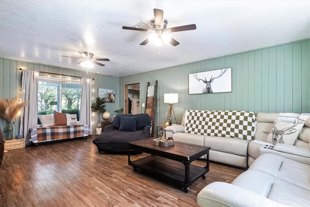 living room featuring wooden walls, ceiling fan, wood-type flooring, and a textured ceiling