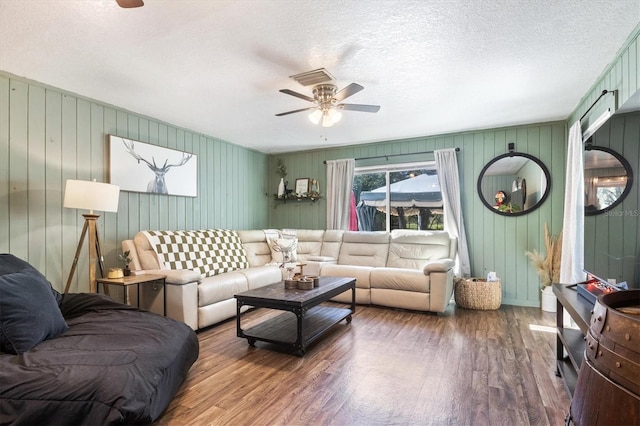 living room with wooden walls, ceiling fan, dark wood-type flooring, and a textured ceiling