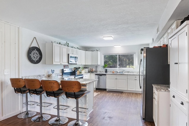 kitchen featuring kitchen peninsula, wood-type flooring, stainless steel appliances, and white cabinetry