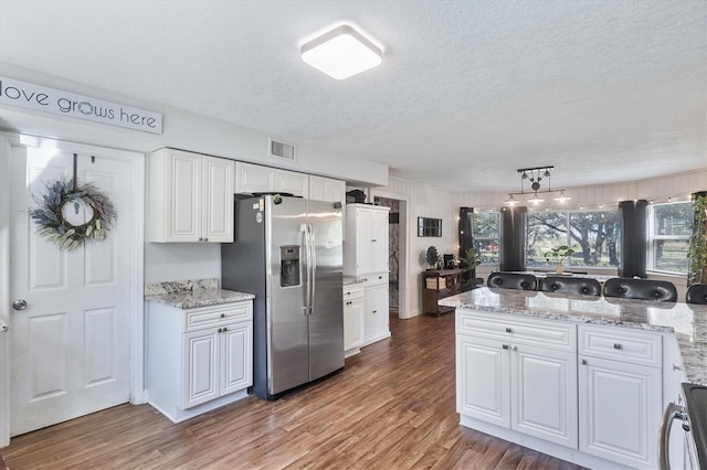 kitchen featuring pendant lighting, hardwood / wood-style flooring, a textured ceiling, white cabinetry, and stainless steel appliances