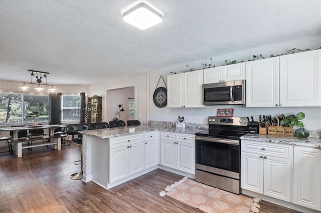 kitchen featuring white cabinets, hanging light fixtures, dark hardwood / wood-style floors, appliances with stainless steel finishes, and kitchen peninsula