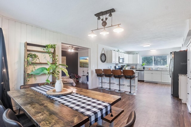 dining space with a textured ceiling, dark hardwood / wood-style flooring, ceiling fan, and wooden walls