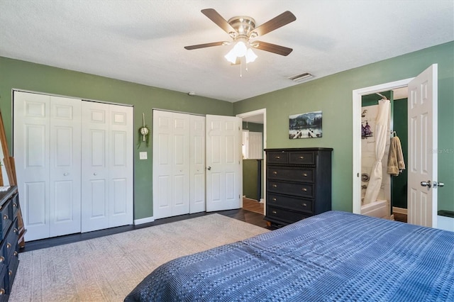 bedroom with ensuite bath, ceiling fan, dark hardwood / wood-style floors, a textured ceiling, and two closets