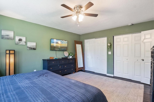 bedroom with hardwood / wood-style flooring, ceiling fan, a textured ceiling, and two closets