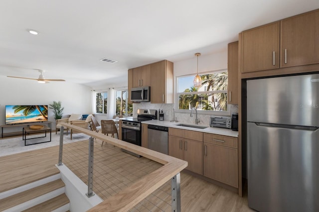 kitchen with backsplash, sink, appliances with stainless steel finishes, decorative light fixtures, and light hardwood / wood-style floors