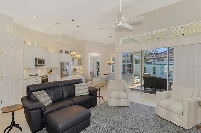 living room featuring ceiling fan with notable chandelier, light tile patterned flooring, and high vaulted ceiling