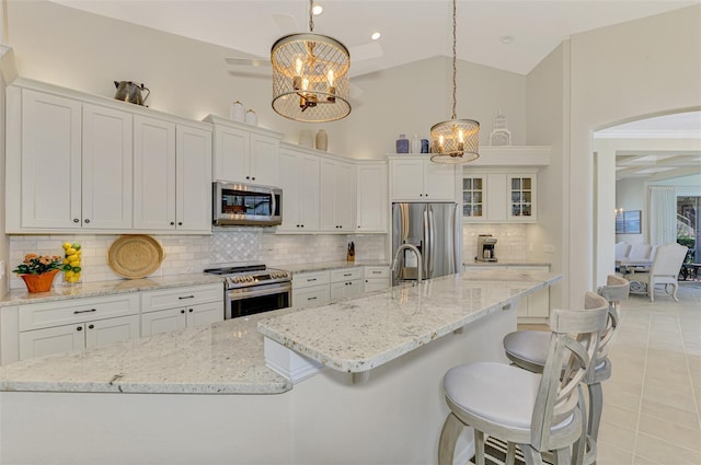 kitchen with tasteful backsplash, white cabinetry, stainless steel appliances, and decorative light fixtures