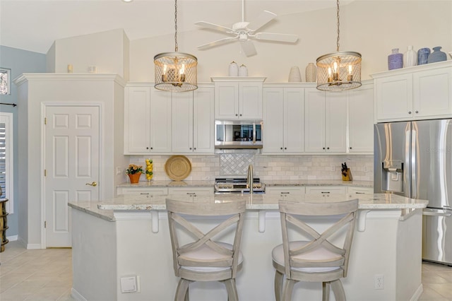 kitchen with light tile patterned floors, stainless steel appliances, decorative backsplash, white cabinetry, and an island with sink