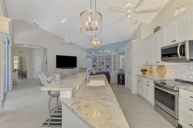 kitchen featuring appliances with stainless steel finishes, a breakfast bar, open floor plan, a sink, and ceiling fan with notable chandelier