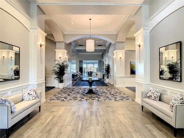 foyer featuring arched walkways, light wood finished floors, a decorative wall, ornamental molding, and wainscoting