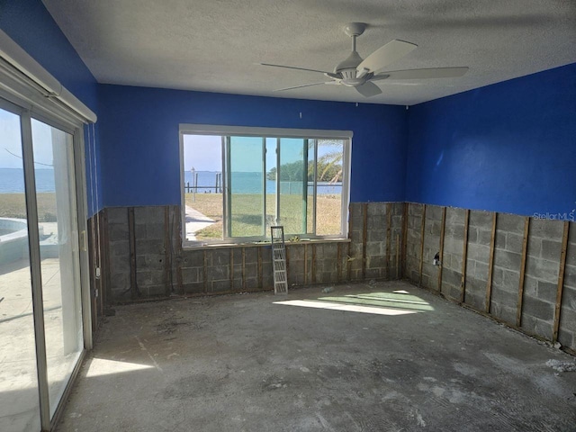 unfurnished room featuring a textured ceiling, a water view, ceiling fan, and tile walls