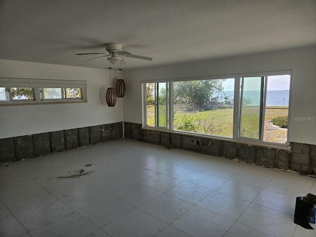 empty room featuring a textured ceiling, a water view, and ceiling fan