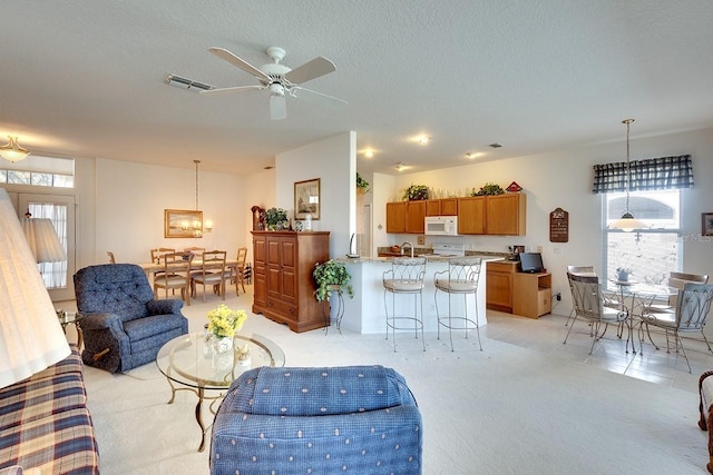 living room featuring ceiling fan with notable chandelier, light colored carpet, and a textured ceiling