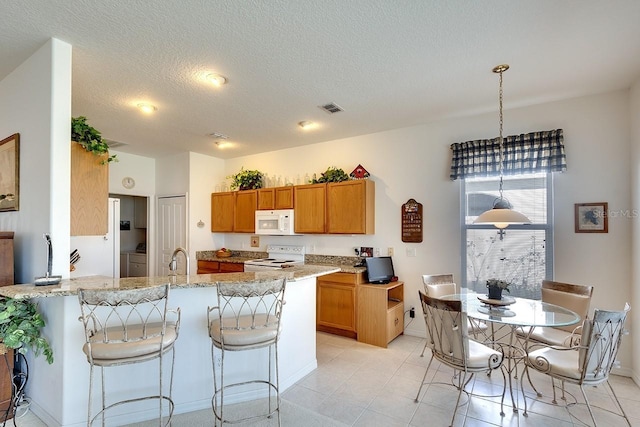 kitchen featuring white appliances, hanging light fixtures, light stone countertops, a textured ceiling, and kitchen peninsula