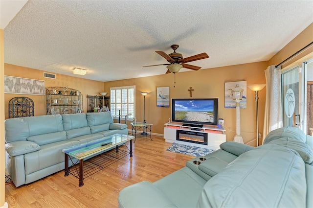 living room featuring ceiling fan, light hardwood / wood-style flooring, and a textured ceiling