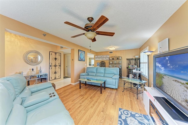 living room with ceiling fan, a textured ceiling, and light hardwood / wood-style flooring