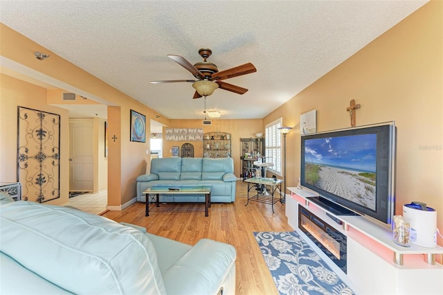 living room featuring ceiling fan, light wood-type flooring, and a textured ceiling