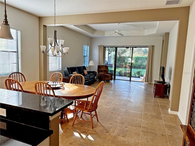 dining room featuring ceiling fan with notable chandelier, a tray ceiling, and light tile patterned flooring