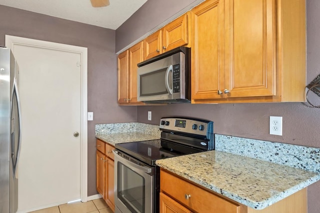 kitchen featuring light stone countertops, light tile patterned floors, stainless steel appliances, and ceiling fan