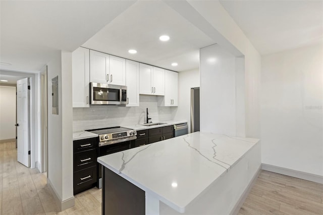 kitchen with kitchen peninsula, stainless steel appliances, sink, white cabinets, and light hardwood / wood-style floors