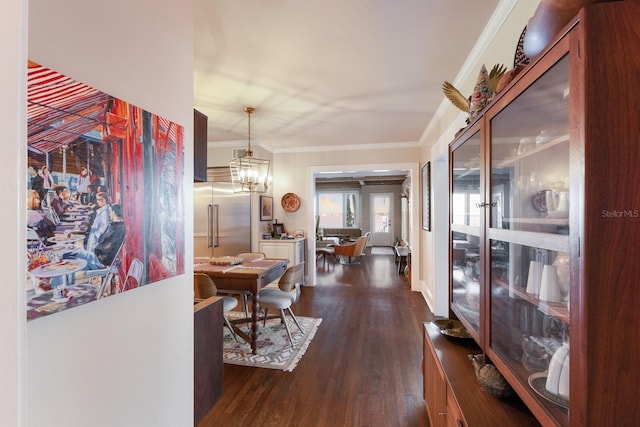 hall featuring dark wood-type flooring, ornamental molding, and a notable chandelier