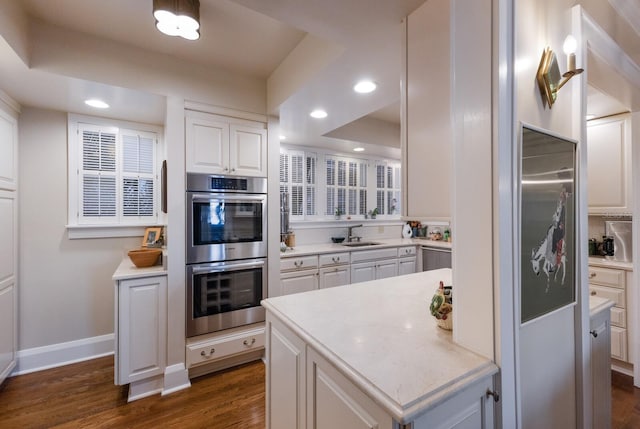 kitchen with white cabinets, appliances with stainless steel finishes, dark wood-type flooring, light countertops, and a sink