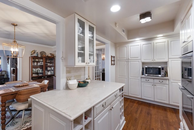 kitchen featuring pendant lighting, light countertops, stainless steel microwave, glass insert cabinets, and white cabinets