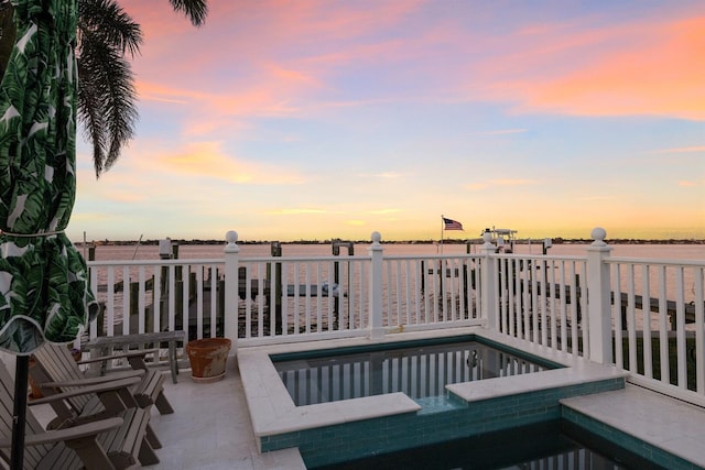 pool at dusk with a water view and a hot tub