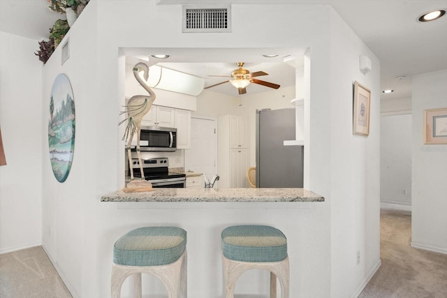 kitchen featuring light carpet, ceiling fan, appliances with stainless steel finishes, light stone counters, and kitchen peninsula