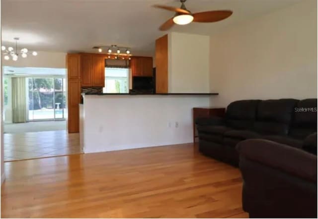 living room with ceiling fan with notable chandelier and light hardwood / wood-style flooring