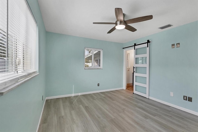 unfurnished bedroom featuring a barn door, ceiling fan, and light hardwood / wood-style floors