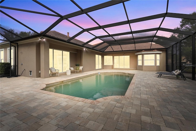 pool at dusk with a patio area, glass enclosure, and an outdoor pool