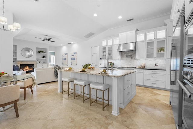 kitchen with a breakfast bar, a glass covered fireplace, white cabinetry, and under cabinet range hood