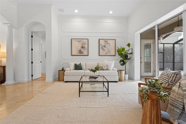 living room featuring arched walkways, ornamental molding, decorative columns, and baseboards