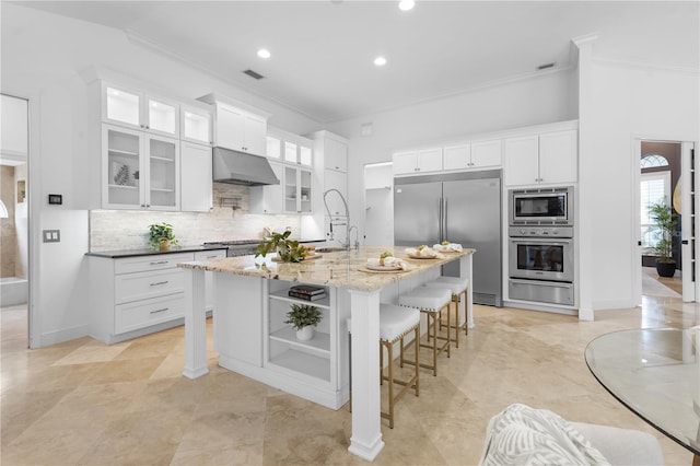 kitchen with a warming drawer, ornamental molding, built in appliances, under cabinet range hood, and a kitchen bar