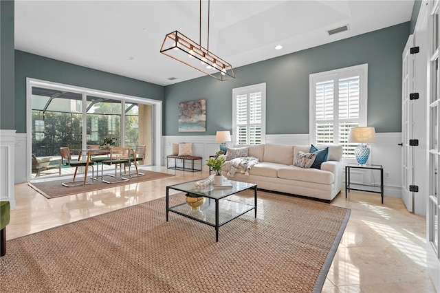 living room featuring marble finish floor, plenty of natural light, visible vents, and a decorative wall