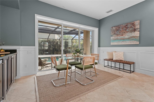 dining area with light tile patterned floors, a decorative wall, a wainscoted wall, visible vents, and a sunroom