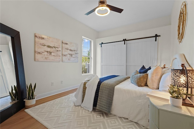 bedroom with light wood-type flooring, ceiling fan, baseboards, and a barn door